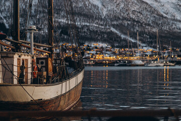 A classic wooden ship is moored in a quiet harbor with a backdrop of a city and snow-covered...