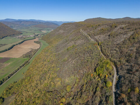 Aerial view of a winding road snakes through a forested hillside, contrasting with the open fields and distant mountains, Ple&Aring;&iexcl;ivec, Ko&Aring;&iexcl;ice Region, Slovakia.