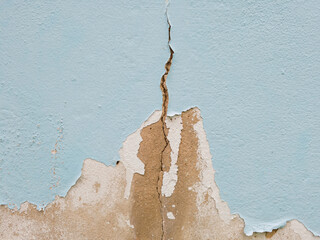 Close-up light blue painted wall with large, peeling sections revealing gray, rough concrete...