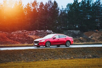 Fototapeta premium Red sedan driving along wet road near forest