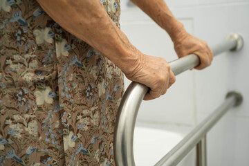Asian elderly woman patient use toilet support rail in bathroom.