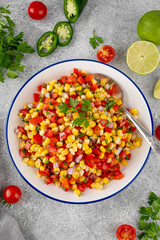 Corn salsa in a bowl with lime, jalapeno pepper, fresh herbs and tortilla chips on a concrete background. Mexican cuisine. Healthy food.