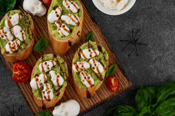 Halloween food. Avocado toasts with mozzarella in the shape of skulls and balsamic sauce on top. Funny food idea. Top view, copy space.