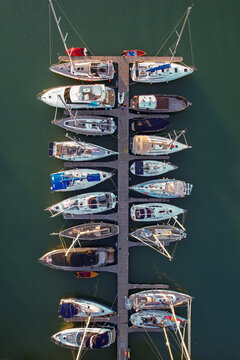 Aerial view of boats moored tightly along a pier, their hulls reflecting the light, creating a striking contrast against the dark water, Venice, Veneto, Italy.