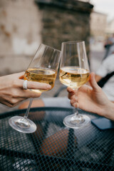 Two friends celebrating with toast of white wine glasses at outdoor cafe, savoring moment of togetherness and relaxation while enjoying vibrant summer atmosphere. Friends toasting white wine glasses