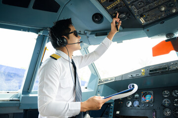 Professional airline pilot in uniform inspecting cockpit control panels during safety checks, ideal for aviation, travel, and airline safety themes. © Nuttapong punna
