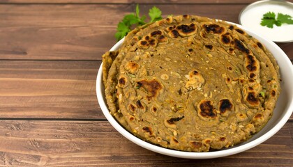 A delicious, round flatbread, speckled with flecks, sits in a white bowl, set against a dark wooden table.