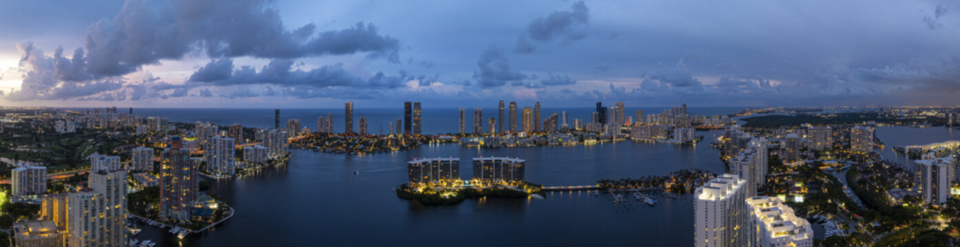 Aerial view of the illuminated coastal skyline contrasting against the dark waters of Dumfoundling Bay, with buildings reflecting the night sky, Aventura, Florida, United States.