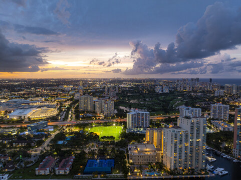 Aerial view of illuminated buildings casting golden glows against the deepening blues of twilight in the vibrant cityscape, Aventura, Florida, United States.