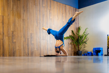 Yoga instructor performing headstand in modern studio with wooden wall