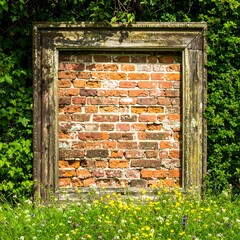 A weathered wooden frame surrounds a vibrant brick wall, nestled amidst a field of wildflowers.