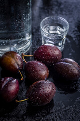 Plums and distilled alcohol on black table. Plum brandy shot.