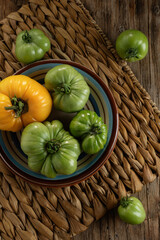 Freshly harvested green and yellow heirloom tomatoes arranged on a rustic wooden table with woven placemat