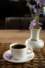 Elegant coffee cup resting on a woven mat beside a vase with fresh purple flowers in a warm cafe setting