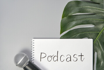 Microphone and notebook with podcast text on gray background featuring large green leaf.
