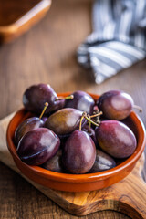 Ripe plums in bowl on wooden table.