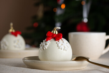 Christmas ball cakes with red bows and snowflakes with cup of tea on a table with a Christmas tree in the background. Vertical orientation.
