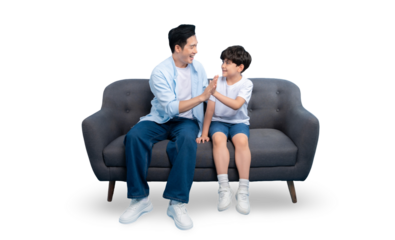 A father and son sharing a moment of connection while sitting on a sofa. They are dressed in casual attire, creating a relatable and heartwarming scene on a solid background.