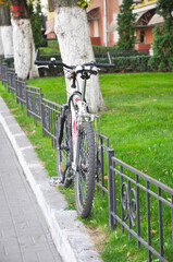 The bicycle is chained to a metal fence outside for safety.