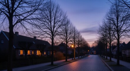 Obraz premium Tranquil suburban street at dusk with illuminated houses and bare trees. Cozy neighborhood scene with warm lights in windows. Peaceful evening atmosphere for postcard or wallpaper