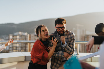 Business people enjoying music and laughter on a high-rise balcony at sunset, celebrating success and teamwork in an urban setting. Uplifted spirits and camaraderie shine through this joyful moment.