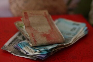 Stacked and folded Indian rupee notes on a red background, used as a sacred offering during worship, puja ceremonies, and cultural traditions.