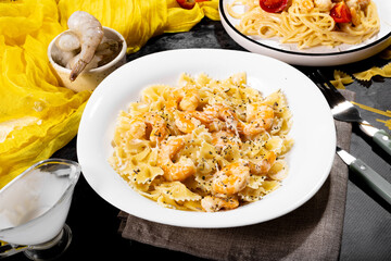 Two plates of creamy Italian pasta with shrimp and cheese, spaghetti and farfalle, styled on a dark rustic background. Delicious seafood dinner.