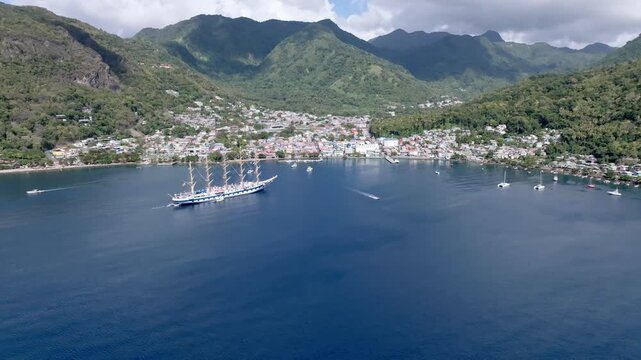 Aerial view of a majestic sailing ship cutting through the deep blue waters near the town nestled by lush green mountains, Le Pitons, Soufri&egrave;re, Saint Lucia.