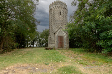 Der Bismarckturm aus Naturstein steht zwischen dichtem Grün. Über dem massiven Turm ziehen dunkle Wolken auf und verleihen der Szene eine eindrucksvolle, fast dramatische Stimmung.