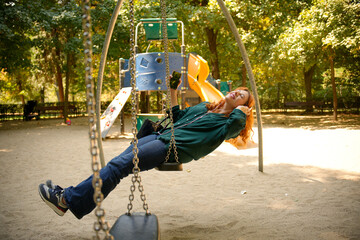 Woman listening music and relaxing on swing in playground