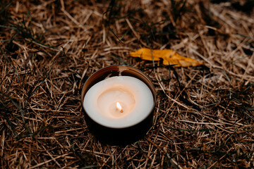 Candle burning in autumn grass under the rain, wet leaves around, cozy and atmospheric fall scene.