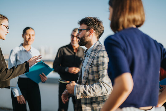 Diverse group of business colleagues gathering on a high-rise balcony, sharing ideas and celebrating together at sunset. The image captures a friendly and collaborative atmosphere in a cityscape