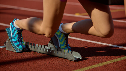 Athlete poised at starting blocks on track in blue running shoes with calm focus. Concept of...