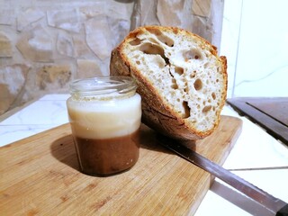 Homemade roasted lard in a jar, a piece of fresh sourdough bread, and a knife on a wooden cutting...