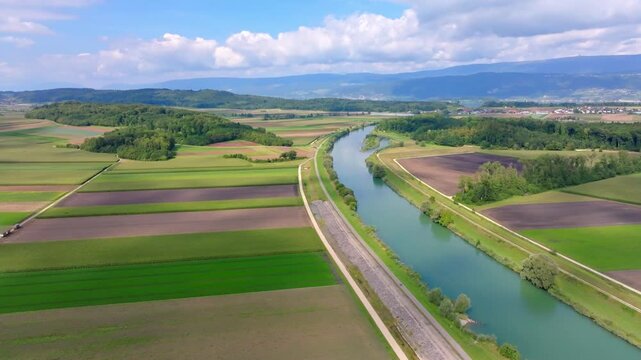 Aerial view of the lush green fields, dark forests, and winding river creating a tapestry of contrasting colors, Hagneck, Bern, Switzerland.
