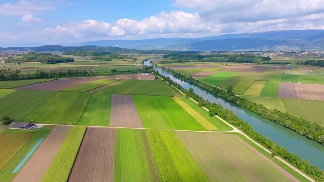 Aerial view of the vivid contrast of the blue canal cutting through the landscape of green and brown fields, Hagneck, Bern, Switzerland.