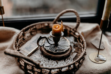 Rustic candle arrangement on a wicker tray by rainy window, warm autumn light creating hygge mood for lifestyle and seasonal projects.