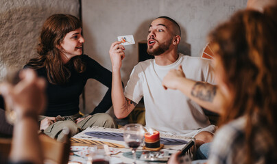 Friends gathered around a table playing a board game, smiling and sharing excitement with each other in a warm, inviting indoor setting.