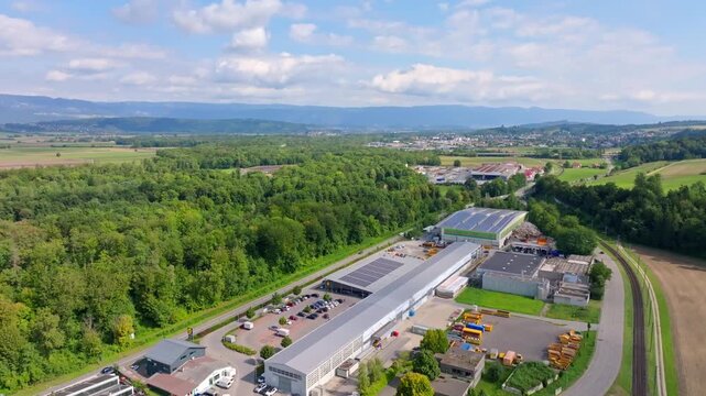 Aerial view of industrial factory with colorful roofs nestled between vibrant green fields and lush forests, Aarberg, Canton of Bern, Switzerland.