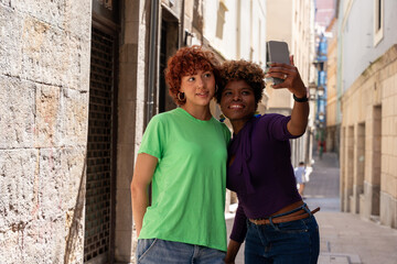Two smiling women taking a selfie in a narrow street