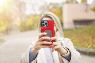 Blonde girl taking selfie on phone outside, autumn sunny day. Photo of a woman walking on her face, talking on a video call with her relatives, a girl in a light coat, autumn, sunny day