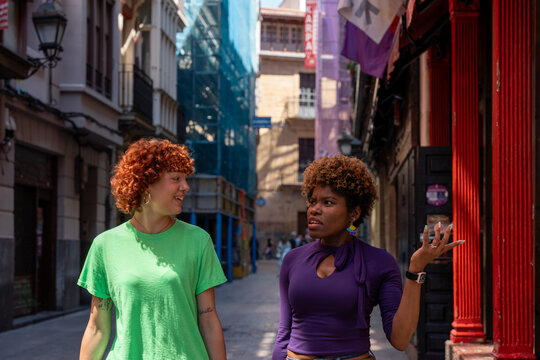 Two young women talking and gesturing in a city street - Powered by Adobe