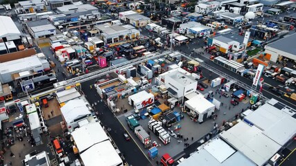 Aerial view of a bustling trade fair, featuring numerous booths and visitors, showcasing various products and services in a busy marketplace.