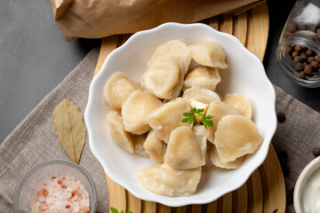 Homemade pelmeni dumplings served hot in ceramic bowl, fresh herbs garnish, dark cozy rustic atmosphere for comfort food.