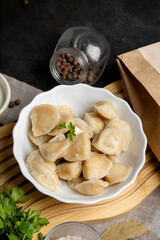 Rustic plate with pelmeni dumplings, topped with parsley and spices, authentic homemade food on dark textured background.