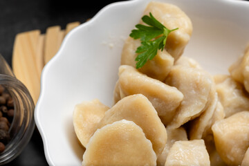 Hot boiled pelmeni with fresh parsley and spices in ceramic bowl, dark rustic food photography with...