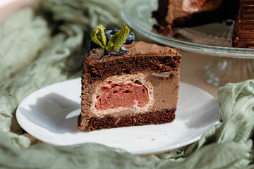 Closeup of chocolate mousse cake with cherry cream layers, topped with blueberry, styled on light...