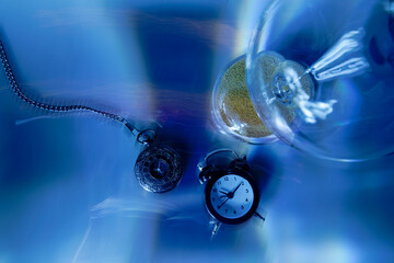 Pocket watch, alarm clock, and hourglass symbolize time passing on blue background, representing...