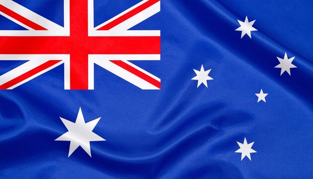 "Australian national flag waving proudly against a partly cloudy sky and distant mountains, showcasing the Union Jack, Commonwealth Star, and Southern Cross constellation."