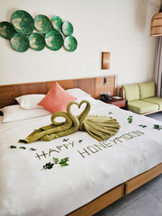 Elegant swan towels grace honeymoon bed, surrounded by verdant leaf artistry, embodying romantic...